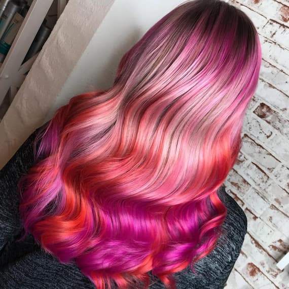 Image of the back of a woman’s head with bold pink rainbow hair color styled in loose waves, created by Wella Professionals.