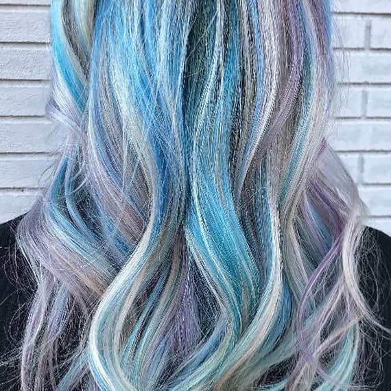 Back of a woman’s head with blue rainbow hair styled in loose waves.