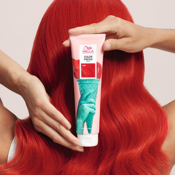 Model with bright red hair holds a Wella Professionals Color Fresh Mask bottle in shade red behind their head.
