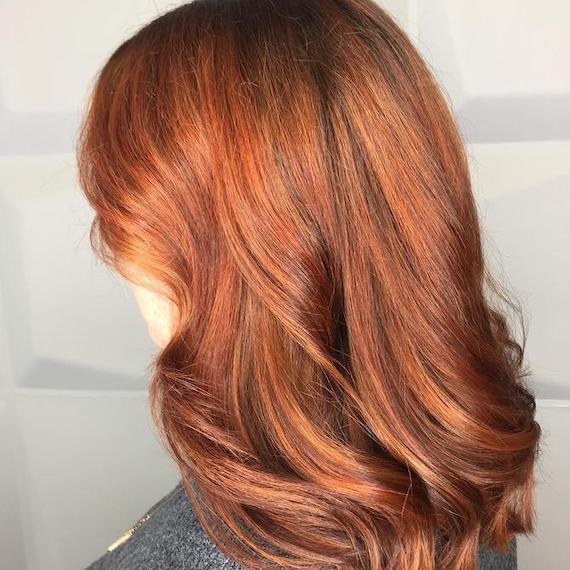 Side profile photo of woman with mid-length copper hair styled in loose curls. Created using Wella Professionals. 