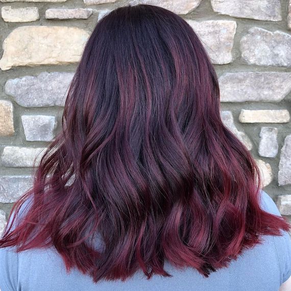 Back of model’s head with mid-length hair featuring red purple balayage. 