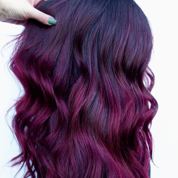 Side profile of model with dark brown roots and red purple balayage.