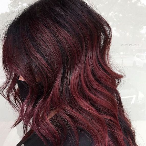 Side profile of model with dark brown roots and raspberry balayage.