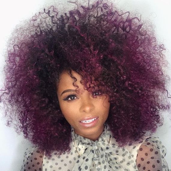 Model faces camera with violet red balayage through curly hair.