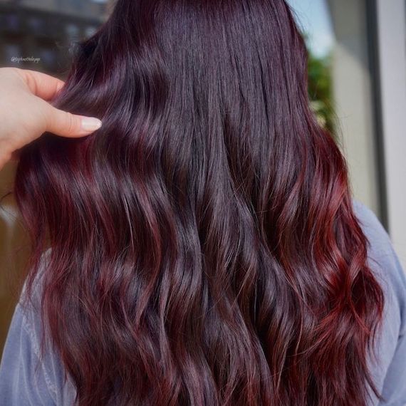 Back of model’s head with long, wavy, red purple balayage hair.