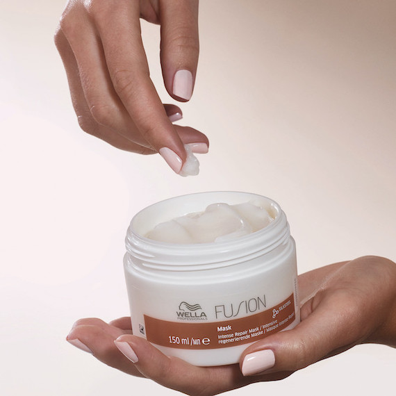 Eine Hand hält eine Dose mit der Wella Fusion Intense Repair Mask in die Höhe.