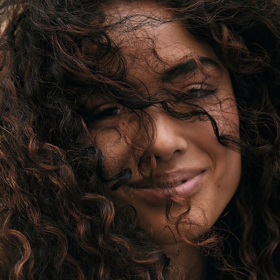 Close-up of woman smiling as brown curly hair brushes over her face.