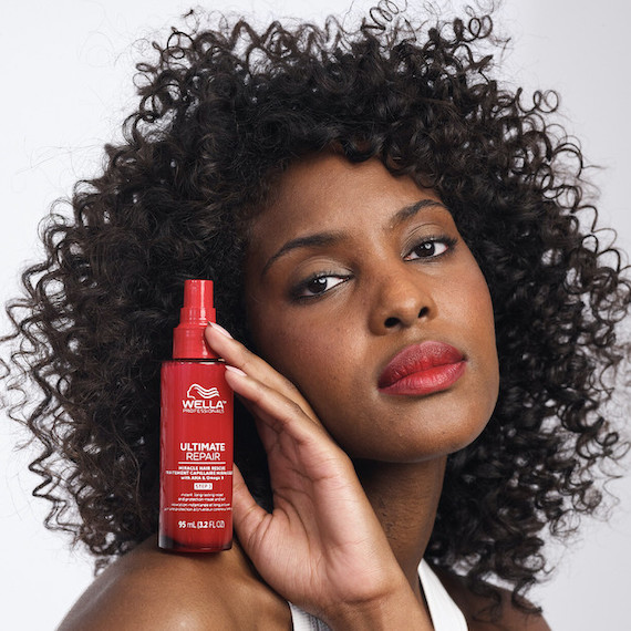 Model with dark brown, curly hair holds a bottle of Ultimate Repair Miracle Hair Rescue Treatment on their shoulder