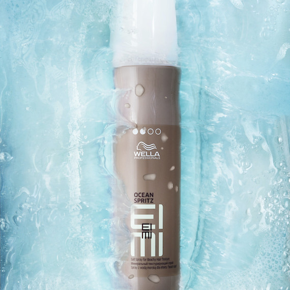 Bottle of EIMI Ocean Spritz salt spray by Wella Professionals emerging from a pool of water