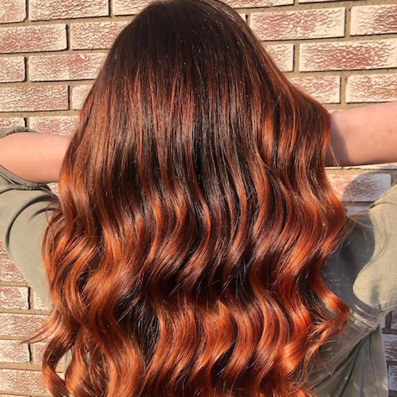 Back of woman’s head with long, wavy, copper red hair and a shadow root, created using Wella Professionals. 