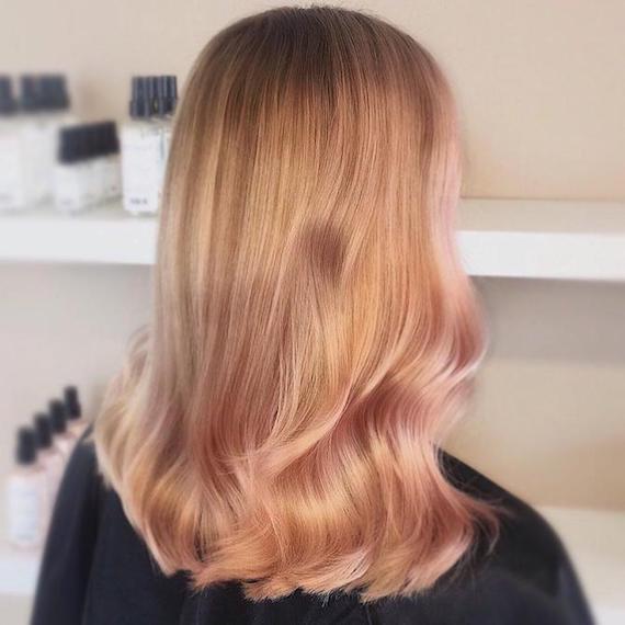 Back of woman’s head showing long, wavy blonde hair with rose gold highlights, created using Wella Professionals. 