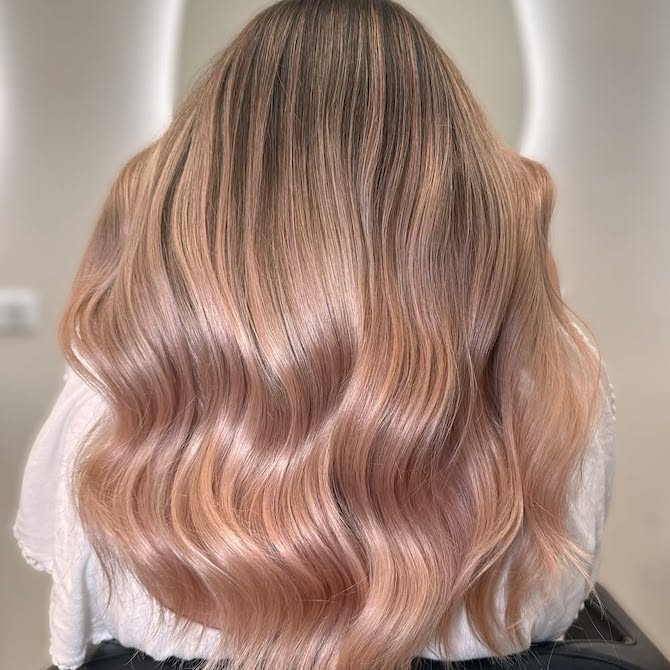 Back of model’s head with long blonde hair featuring a subtle rose gold balayage.