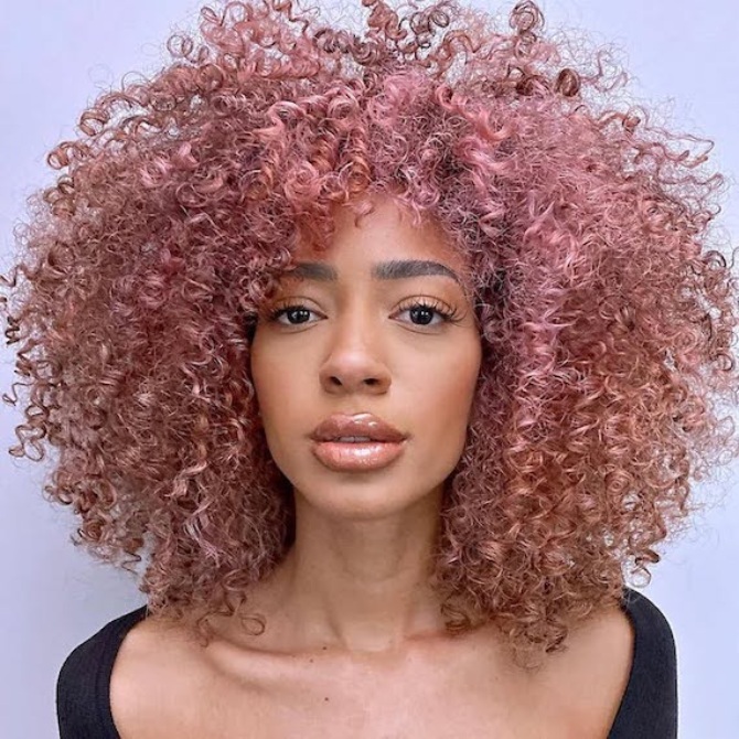 Model with long, curly hair in a radiant rose gold shade.