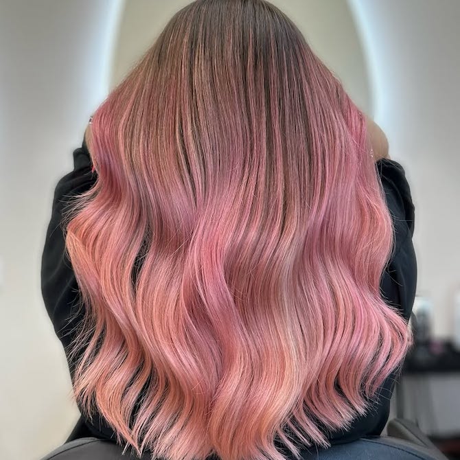 Back of model’s head with long, wavy, dark blonde hair featuring rose gold and bright pink highlights.