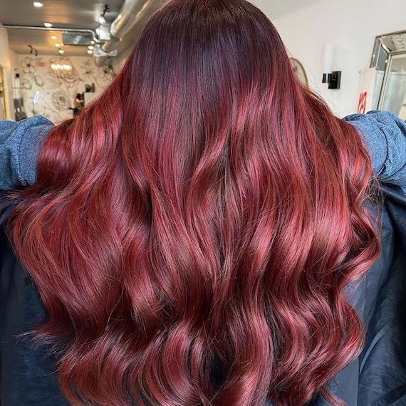 A person facing away from the camera showing their long, wavy ruby raspberry red hair color