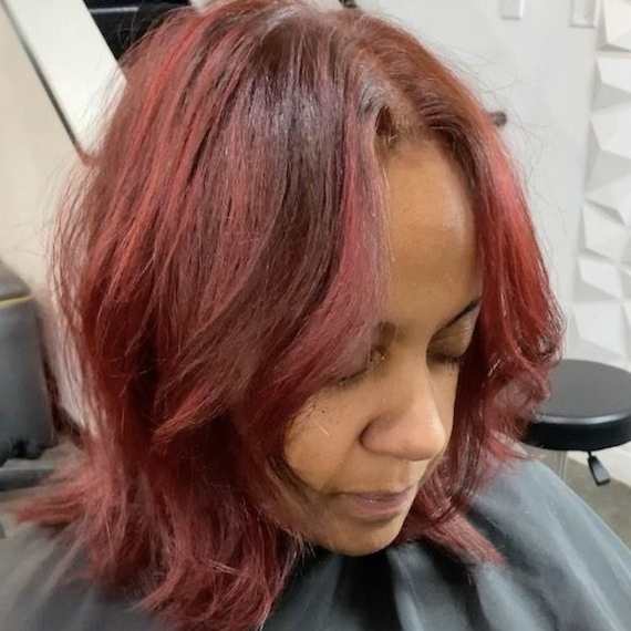 Close-up of a person with ruby red colored hair looking down and wearing a hairdresser's cape