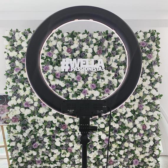 Photography ring light shown against a flower wall backdrop at a Wella Professionals event.