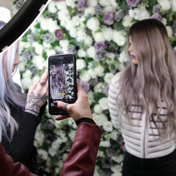 Woman posing against flower wall as she has her photo taken at a Wella Professionals event.