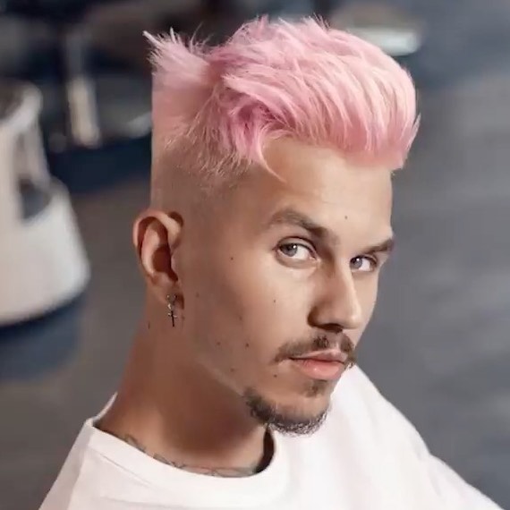 Model with short, pastel pink hair styled in a quiff looks into the camera.