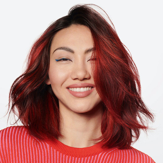 A model with shoulder-length, black and red hair smiles into the camera.