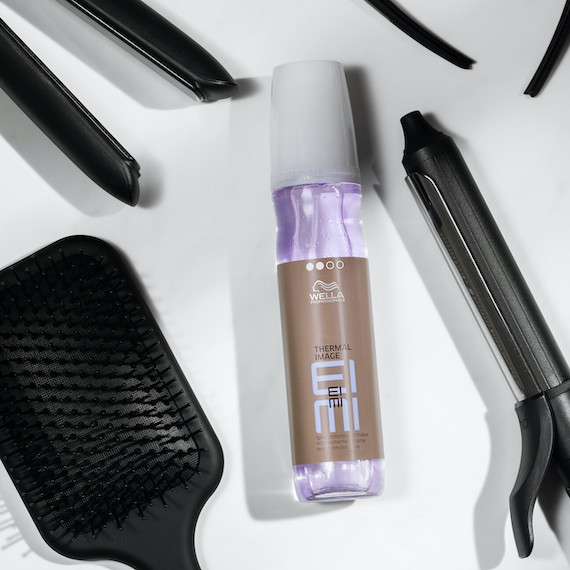 EIMI Thermal Image is on a flat surface, surrounded by a hair brush, straighteners and a curling iron.