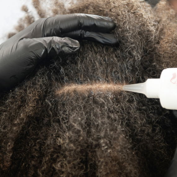 A close-up of Wella Professionals’ Marula Oil Blend Scalp Primer being applied to a woman’s scalp.