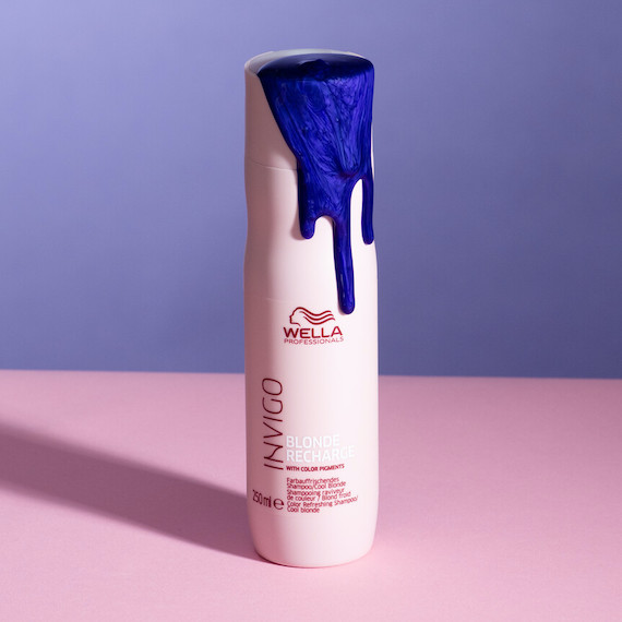 A model’s hand holds a bottle of INVIGO Blonde Recharge Color Refreshing Shampoo.