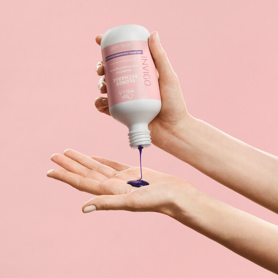 A model pours INVIGO Blonde Recharge Color Refreshing Shampoo into their hand.