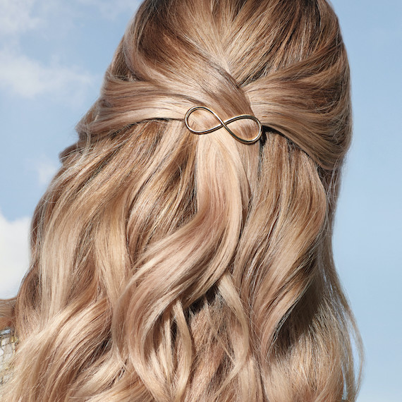 Back of woman’s head showing blonde, glossy hair clipped in a half up style.