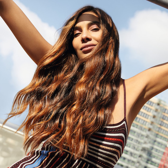 Model facing the camera with long, wavy, glossy brunette hair.