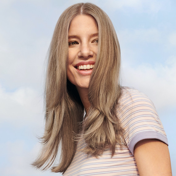 Model smiles at the camera with cool, beige blonde hair.