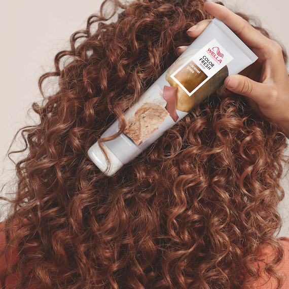 Back of woman’s head with curly brown hair and hand holding the Wella Color Fresh Mask in Caramel Glaze.