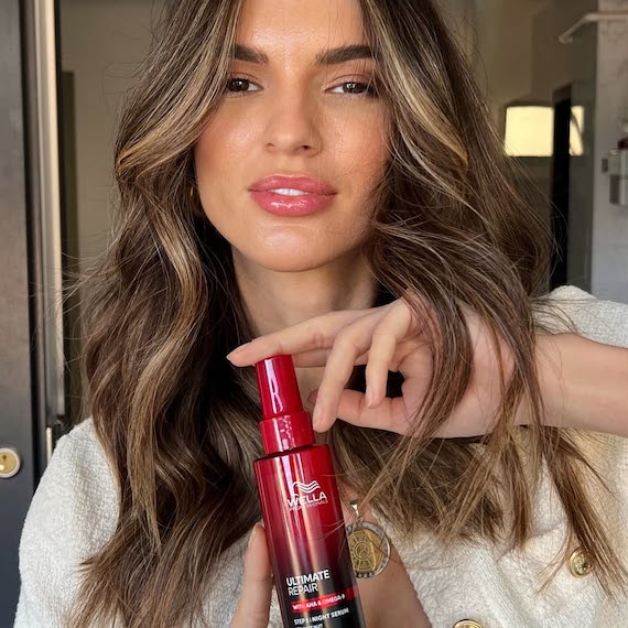 Model with long, light brown, glossy hair holds up a bottle of ULTIMATE REPAIR Night Serum.