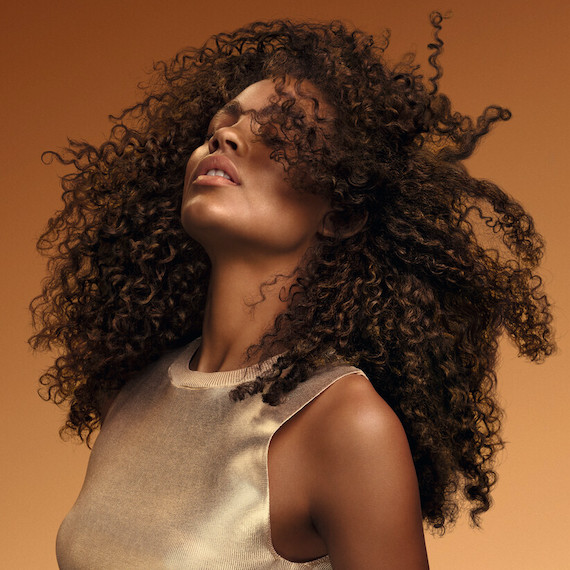 Model tosses their dark brown, glossy, curly hair.