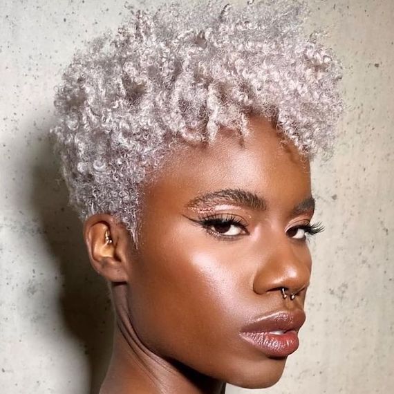 Model faces the camera with short, icy blonde curls and shaved undercut.
