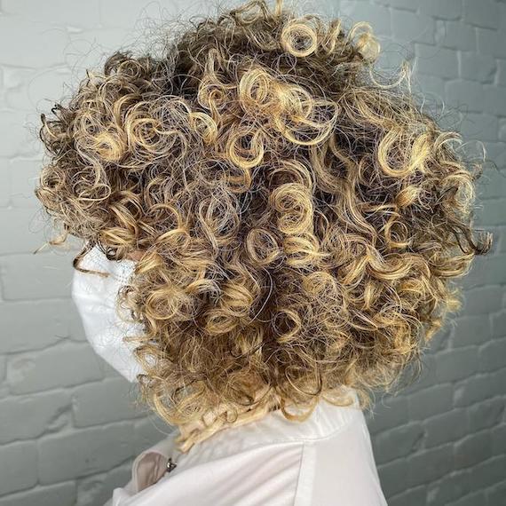 Side profile of model with voluminous, blonde, curly hair.