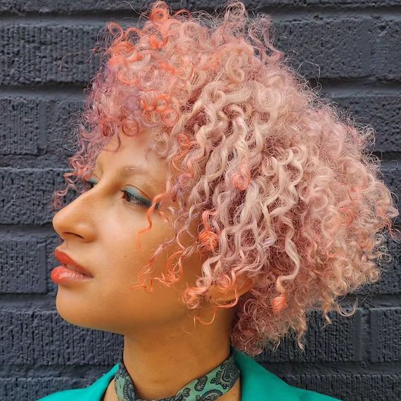 Side profile of model with short, platinum blonde and peach-tinted curly hair