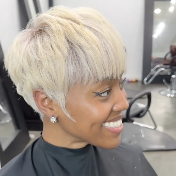 Side profile of model smiling, with short, platinum blonde, pixie haircut and bangs.