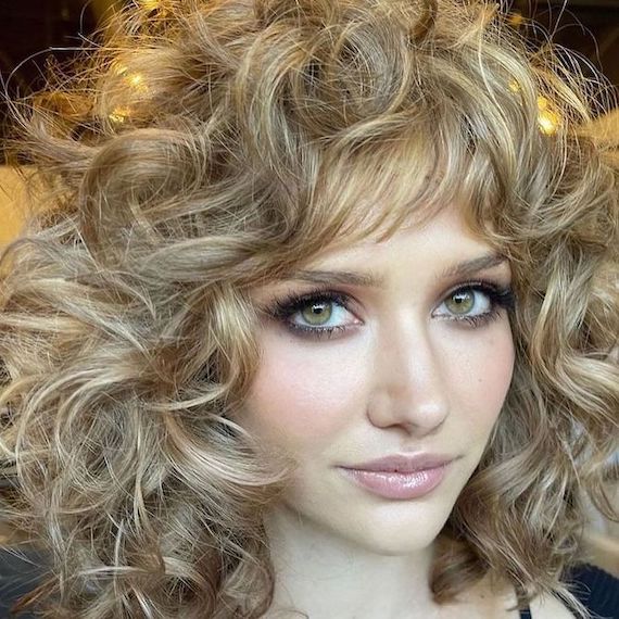 Model with curly, shoulder-length hair featuring golden blonde and light brown highlights.
