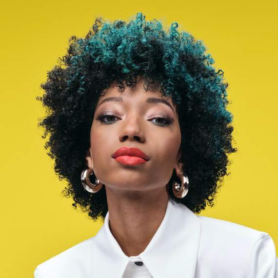 Model with glossy, black, curly hair and a teal green color block through the front.