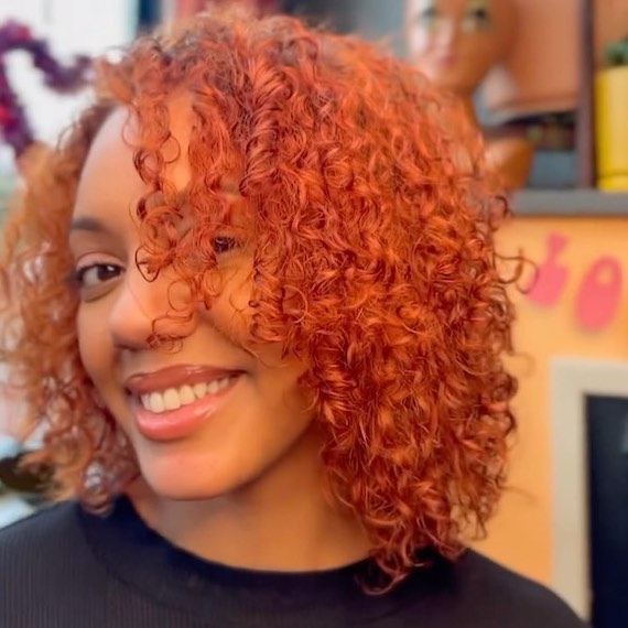 Model with shoulder-length, copper red, curly hair. 