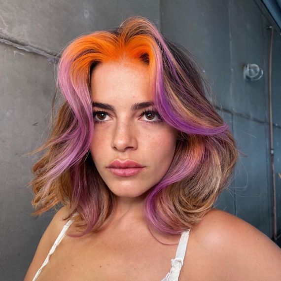Model with wavy, blonde bob featuring a bold-colored orange and purple face frame.