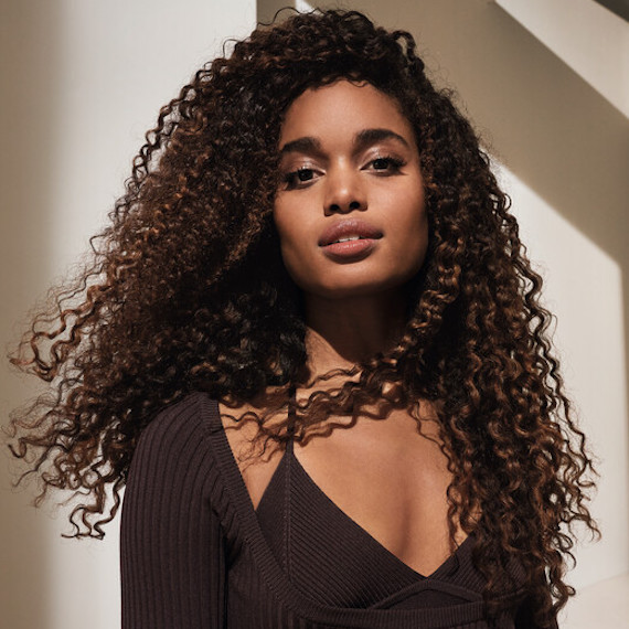 Model with chocolate brown, curly hair faces the camera.