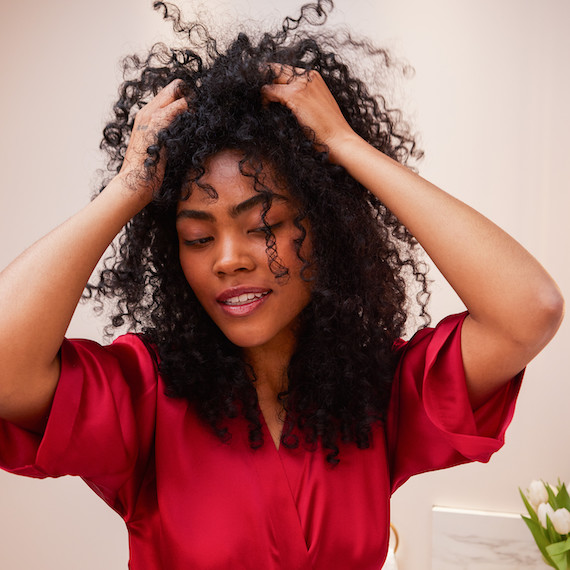 Model smooths ULTIMATE REPAIR Night Serum through their curly hair.