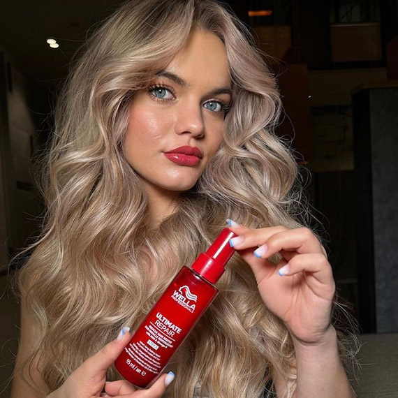 Model with bright blonde, tousled hair holding up a bottle of ULTIMATE REPAIR Miracle Hair Rescue.