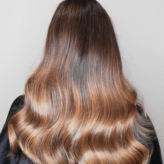 Back of woman’s head with long, wavy, honey brown hair, created using Wella Professionals.