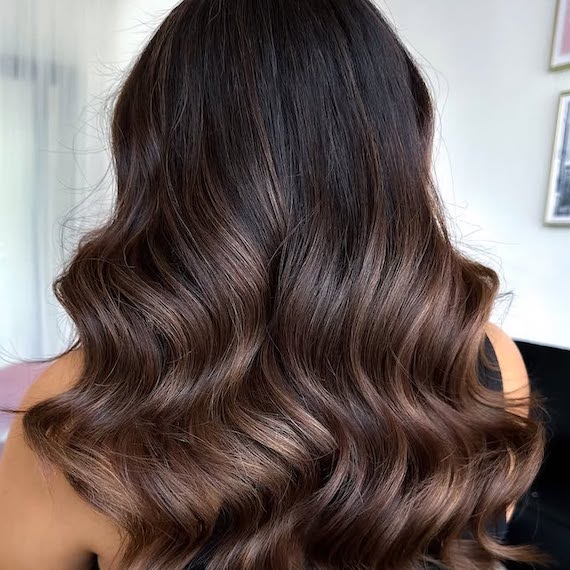 Back of model’s head with long, dark brown, loosely curled hair featuring mocha brown balayage.