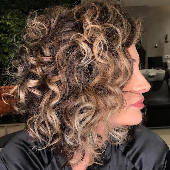 Side profile of woman with curly hair and blonde highlghts, created using Wella Professionals.