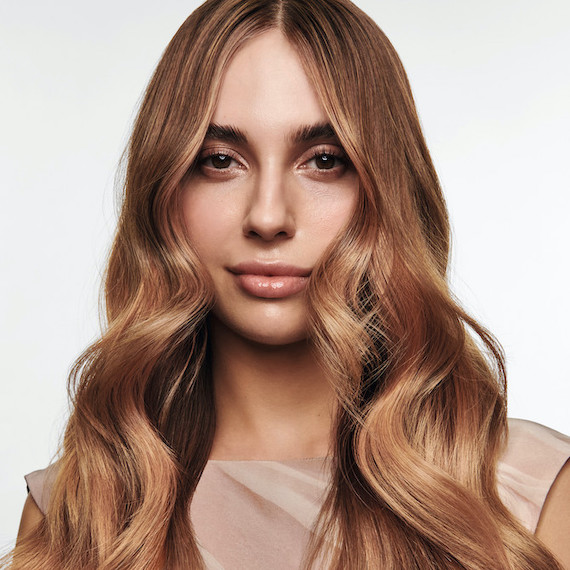 Long, wavy, light brown hair featuring a subtle rose gold balayage.