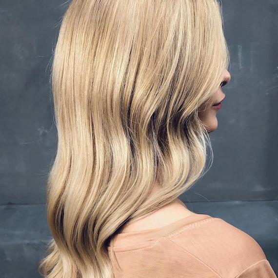 Side profile of woman with long, wavy, buttercream blonde hair, created using Wella Professionals. 